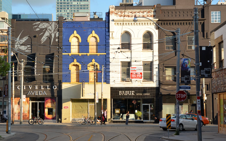 three storey buildings on Queen Street west.  One is a store called Civello, one is a restaurant called Babur and two are empty.