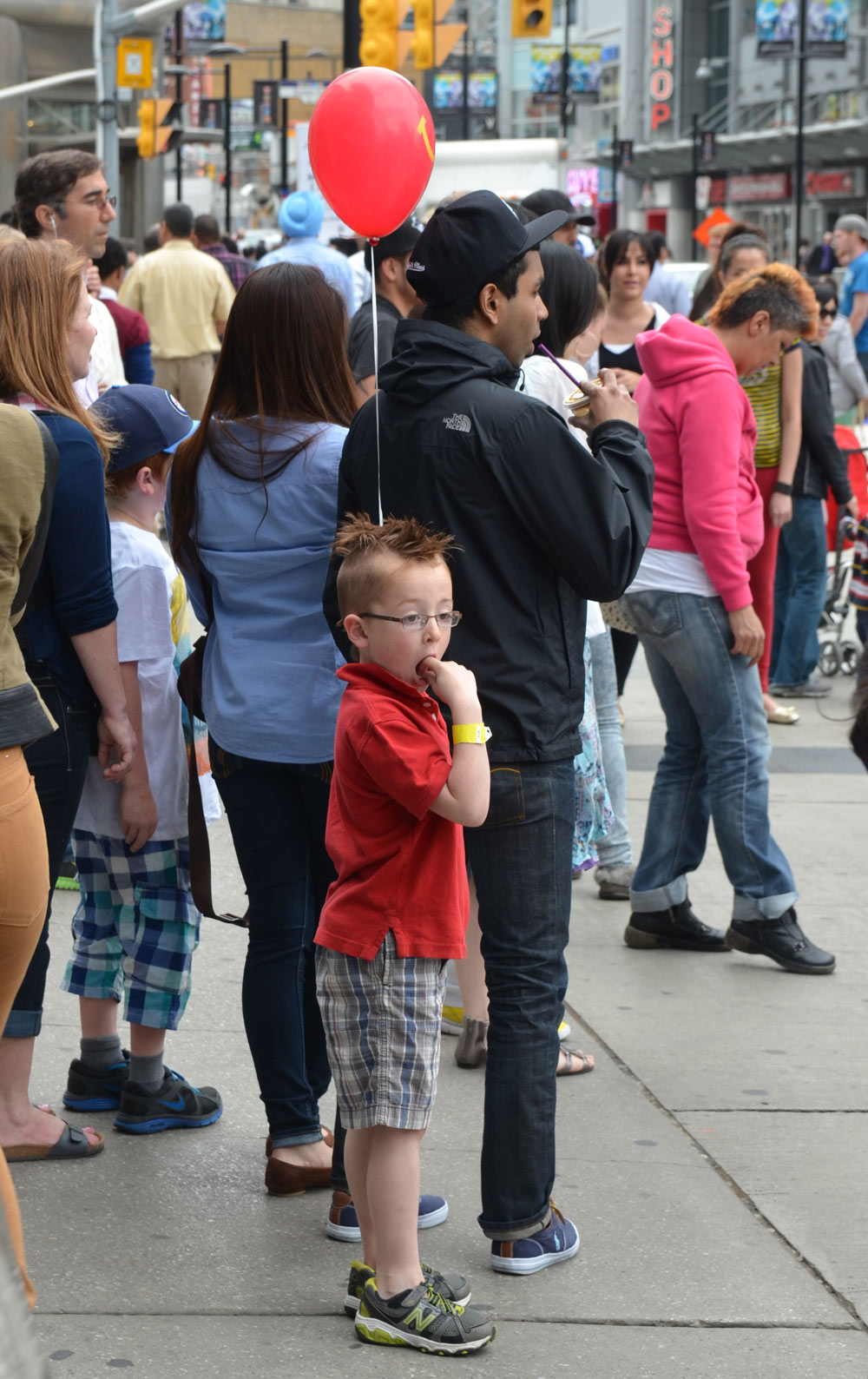 a young boy, standing in a crowd and hold a red balloon on a string