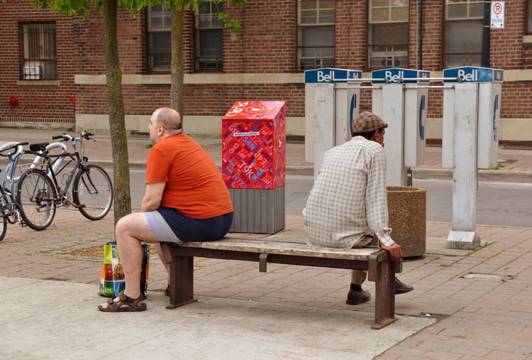 two men, with backs turned, sitting on a concrete bench outside of the Parkdale library