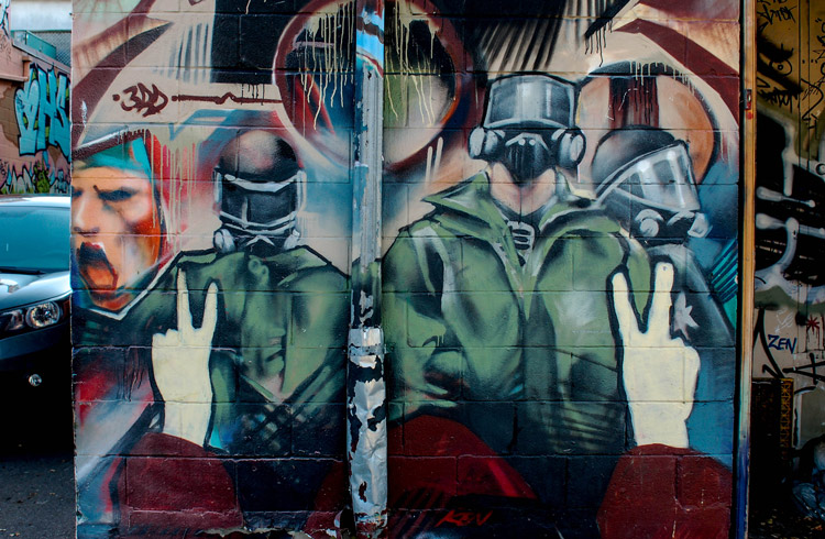 graffiti of policemen in riot gear with a person holding up a peace sign with their fingers in the foreground