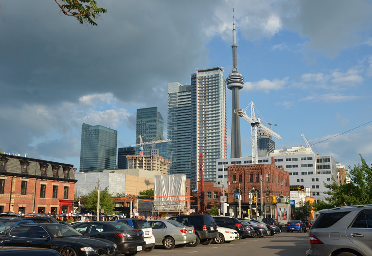 Looking south towards Queen Street West and beyond from Bulwer Street, near Soho Street, stores, parking lot and taller buildings, in the late afternoon sun.