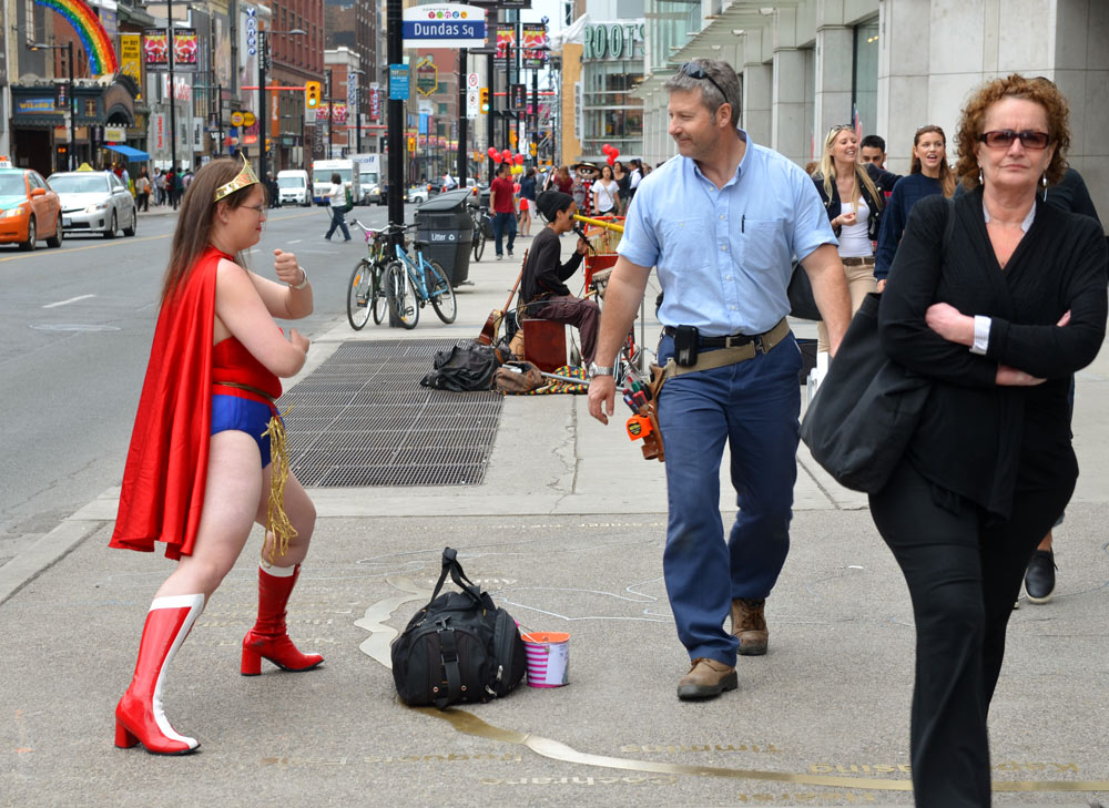 woman dressed in Wonder Woman costume poses on Yonge Street while people walking pass her stop to look and smile