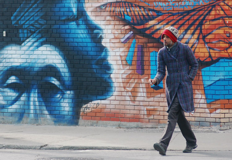 man crossing a road in front of a mural of a man's face and a woman's face
