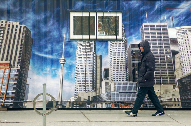 a man walking in front of poster on Dundas Street that shows a downtown Toronto scene, including the CN tower
