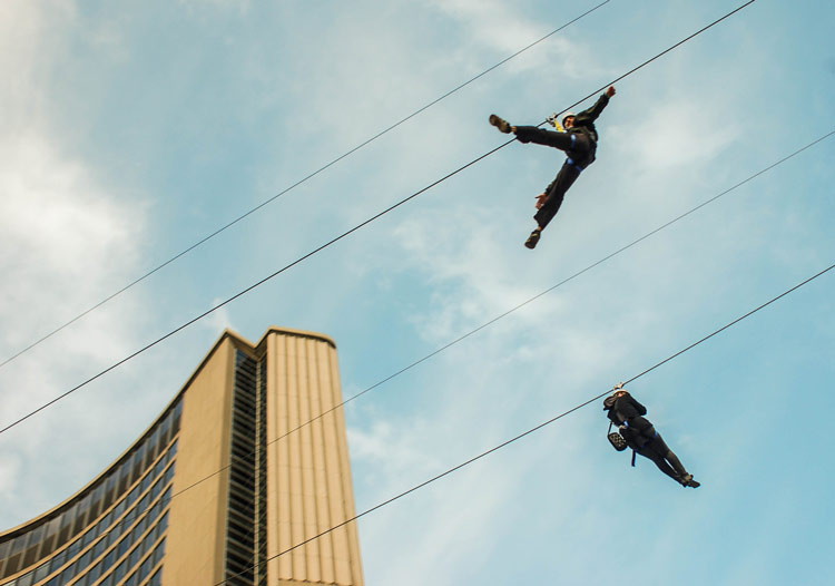 two people going down a 	zipline that was put up over city hall for a few days
