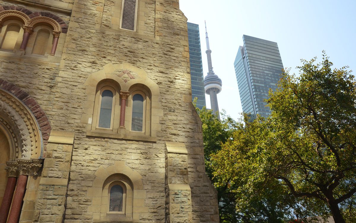 a man is washing the windows of condo building in downtown Toronto, with the CN tower in the background. 