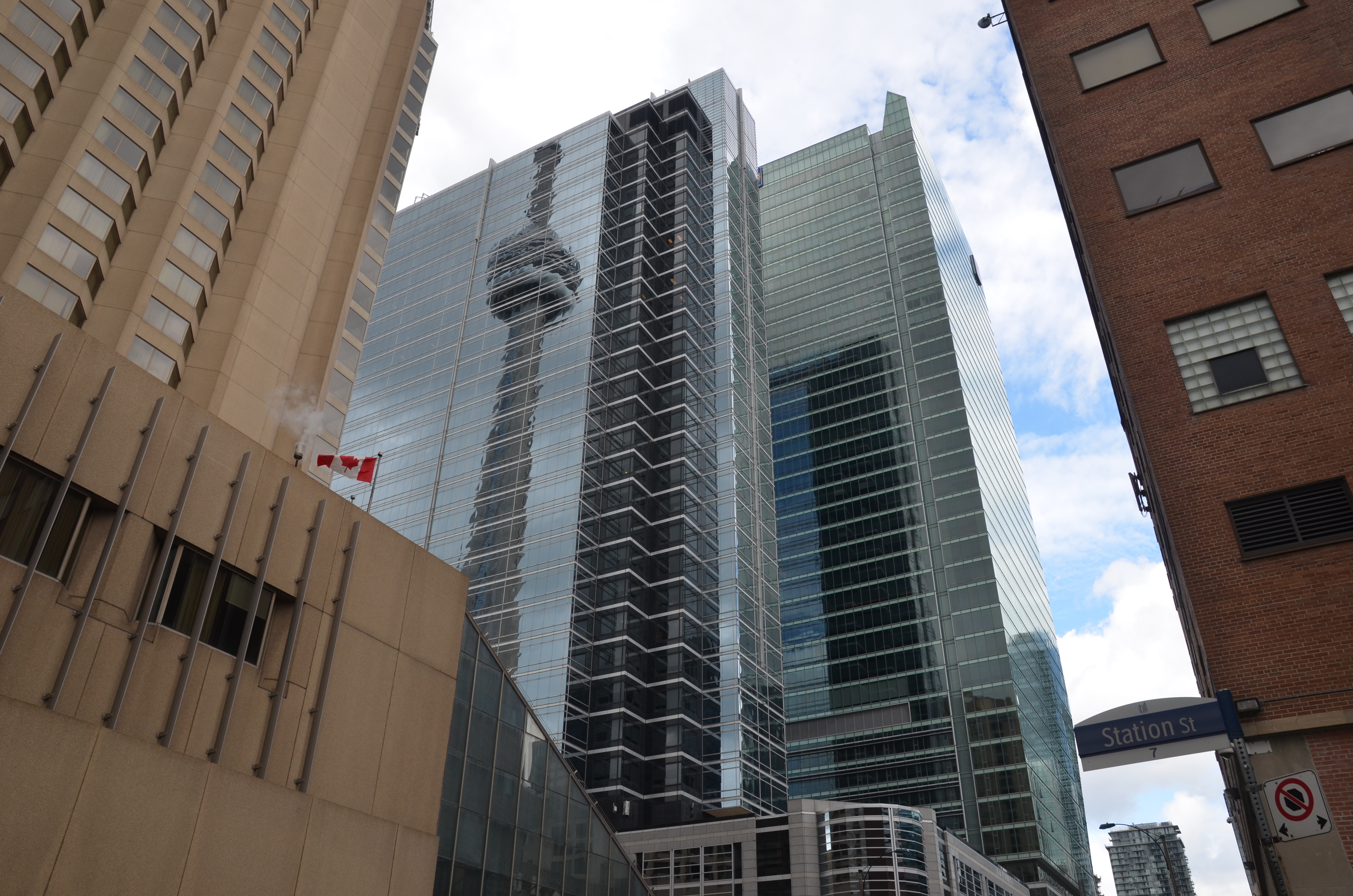 The CN Tower is reflected in a glass window covered building.   