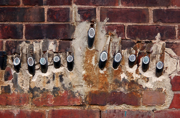 abstract looking picture of an old brick wall.  Several wires that used to exit the building have been cut right at the brick level. 