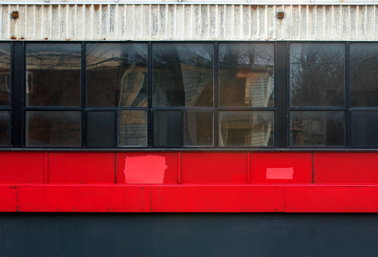 abstract looking picture of a wall that is black at the bottom, has a red stripe under the windows, and has a white metal part across the top of the windows.  