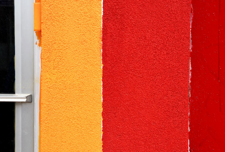 abstract looking picture of a wall that has been painted in vertical stripes of yellow and two tones of red.  Very bright and bold.  