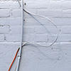 a short copper pipe sticks out of the kerb beside a pale grey wall.  Two wires run down the side of the wall towards the pipe, one metal and one painted the same colour as the wall.   