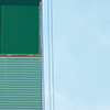 abstract looking picture of wall of a new building that is two tones of green, with a rectangular shape ina darker green.  Light blue sky beside the wall.  