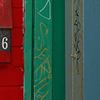 abstract looking picture of a wall beside  a white door.  There is a small section of brick painted bright red, and then some green wood.  The mailbox is on the brick and it too is painted bright red.  The number on the box is 456.  Graffiti tag LSD on the green. 