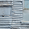 abstract looking picture of an old corrugated metal wall.  what used to be a large window has been covered with metal, and a few small windows have been either painted over or covered from the inside