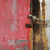 abstract looking picture of an old concrete block wall with streaks of rust.  On either side of the wall is a faded red metal door.  The doors are locked with a chain between them.  