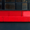 abstract looking picture of a wall that is black at the bottom, has a red stripe under the windows, and has a white metal part across the top of the windows.  