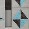 abstract looking picture of part of the exterior wall of the Rex Hotel.  Triangle and diamond shapes are made of turquoise and black tiles, set into grey concrete.  A square window is also  in the picture, with ights that say cafe as well as Amsterdam Brewery.  The cafe sign is half burned out. 