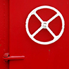 abstract looking picture of the exterior wall of bright red tug boat with a small circular window with a white frame and a white steering wheel.  