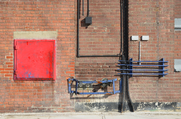abstract looking picture of the side wall of the old Weston Bakery, red brick building with a number of exterior pipes as well as a large red square section 