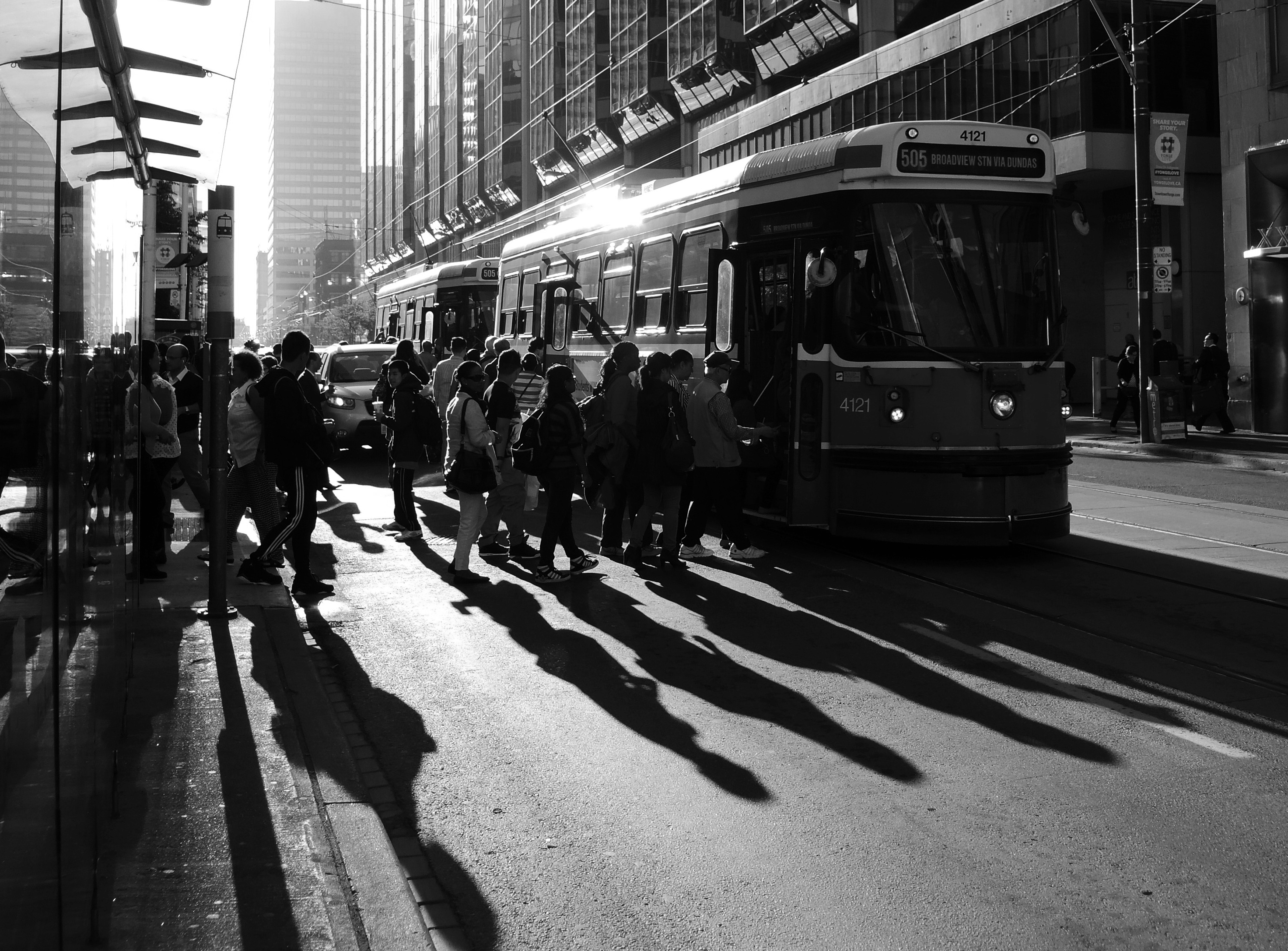 late afternoon, with long shadows, and the setting behind, people getting on a College street TTC streetcar