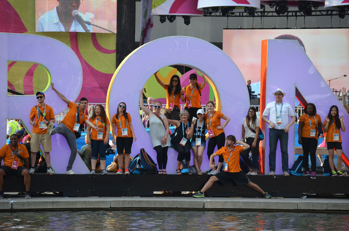 a group of people wearing orange Tshirts pose in front of the Toronto 3D sign at Nathan Phillips Square