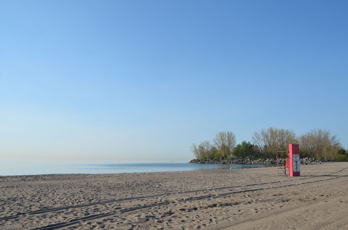 an empty beach on a spring morning, with trees in the distance and an empty red lifeguard stand. 