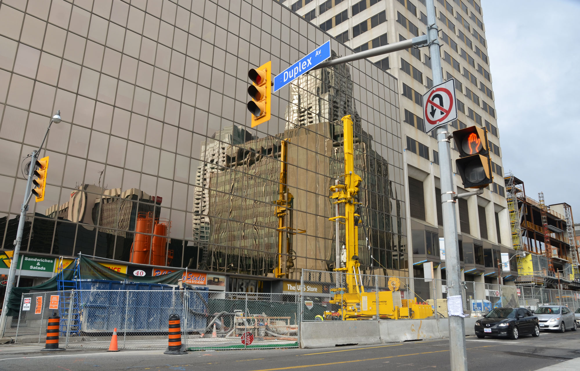 construction on a street in front of a building with reflecting glass, street sign says Duplex Ave, traffic waiting to go through construction area.  