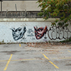 an empty parking lot with an old yello hut for the parking attendant, the far wall of the lot is concrete and has been painted with two graffiti faces