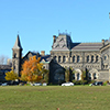 looking across the grass of Kings College circle towards the stone buildings of University College.  The small tree in the foreground has yellow leaves on it. 