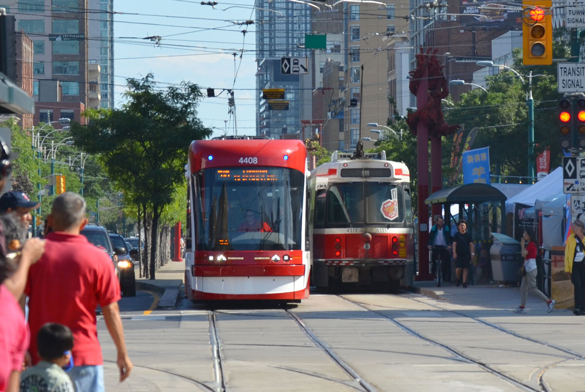 an older streetcar is traveling south and a new streetcar is coming north as they pass each other on Spadina at the intersection with Dundas.  