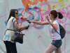 two women try to paint each other with paint rollers while another woman is standing off to the side