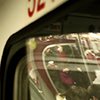 a view of the interior of a subway train.  People sitting, people standing reflected in a mirror, holding coffee cups and talking
