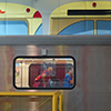 view of a subway car from the side with people in the window.  The subway is in a station and paintings of other subway cars are on the wall 