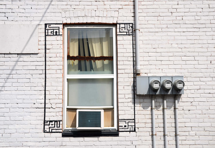 exterior of a white brick building showing a window that has had the outline of shutters drawn around it